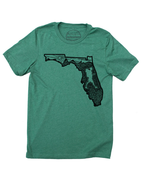 Graphic illustartion of a hiker in state of Florida, complete with rolling hills and setting sun all infill the state. Black ink on a cotton, polyester blend in a green hue. $21.99, free shipping in USA