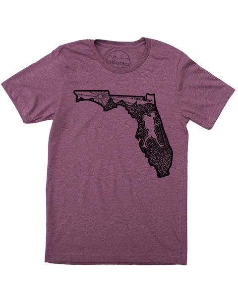 Graphic illustartion of a hiker in state of Florida, complete with rolling hills and setting sun all infill the state. Black ink on a cotton, polyester blend in a plum hue. $21.99, free shipping in USA