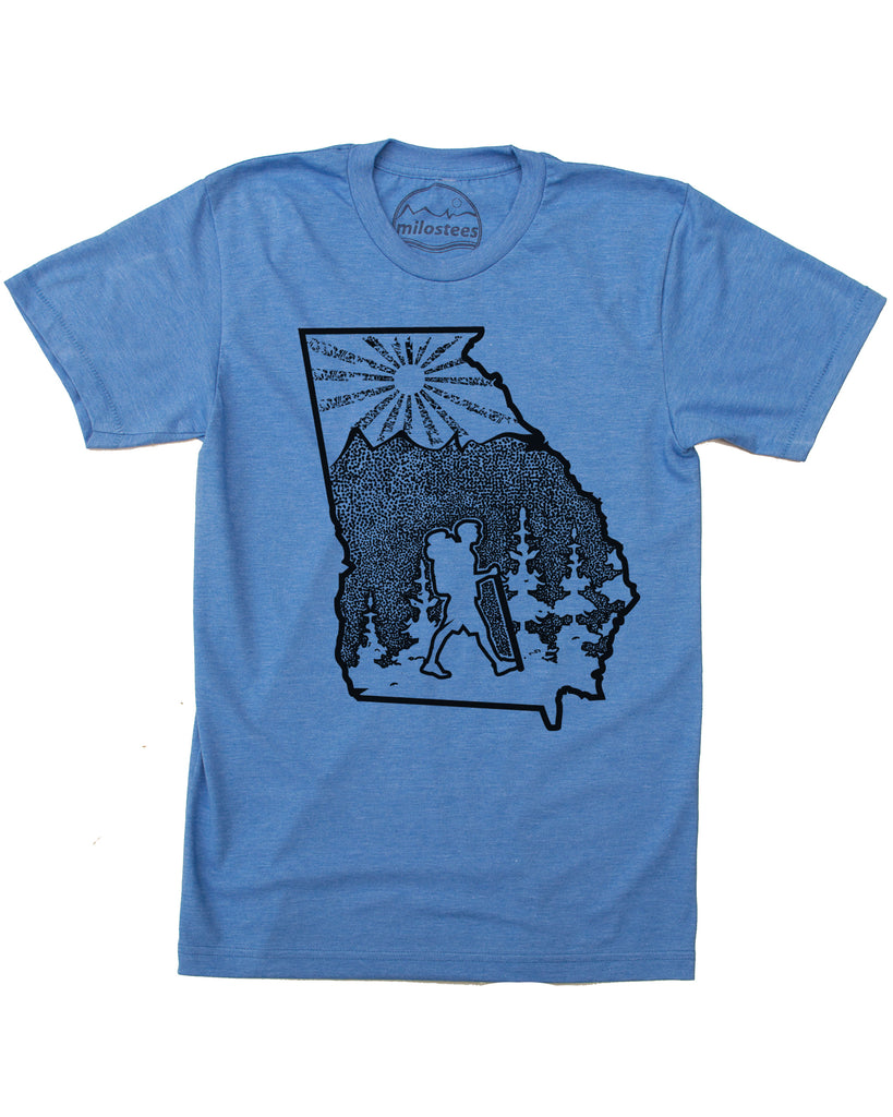 Hand screen printed illustration of a hiker in the state outline of Georgia, the art work also includes trees, mountains, and a setting sun all of which are within the state outline. Black print on a cotton, polyester blend in a blue hue by American Apparel. $21.99, free shipping in the USA.  