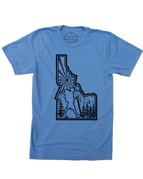 Hike Idaho shirt, blue color, original hand screen printed graphic of a hiker hiking inside the State outline of Idaho, infilled with sun mountains and trees. $21.99, free shipping in the USA.