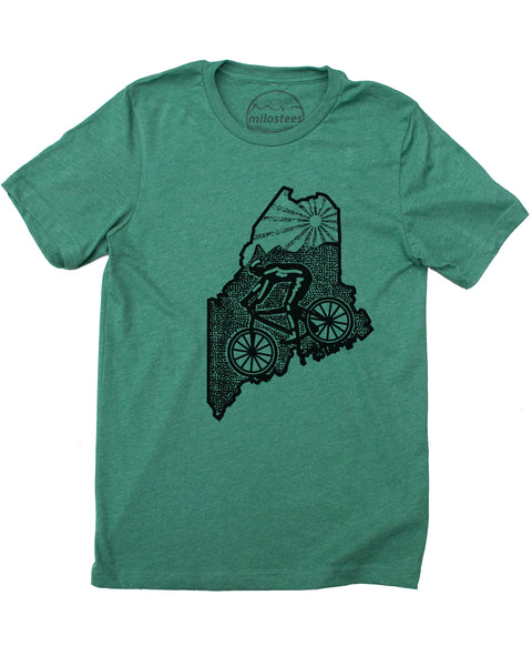 Green cycling t-shirt with a screen-printed design. The design features a cyclist riding along the bottom of the state of Maine. The top third of the design is filled with a mountain logo. A low sun sits in the Maine sky above the mountain logo. The shirt is made from a 52% cotton, 48% polyester blend. Black ink.