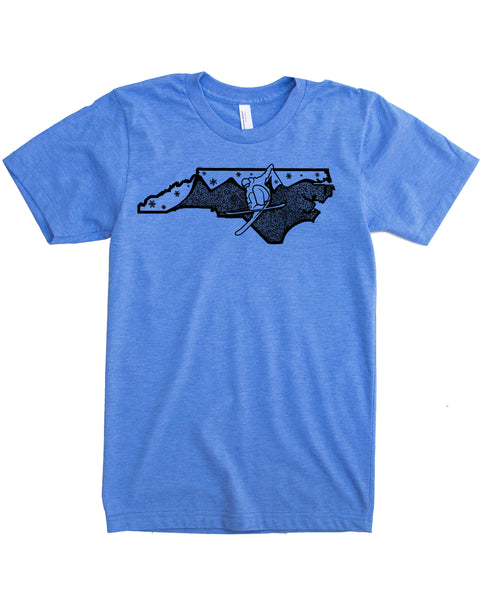 Ski North Carolina graphic, original illustration of a skier pulling an iron cross with the Blue Ridge Mountains in the background and snow in the sky. All graphic elements infill NC. Hand screen printed with black ink on soft cotton, polyester blend in blue.. 